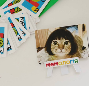 Настольная игра Мемологія от Sovabooks для вечеринки и развлечений, изображение с коробкой и игровыми компонентами.