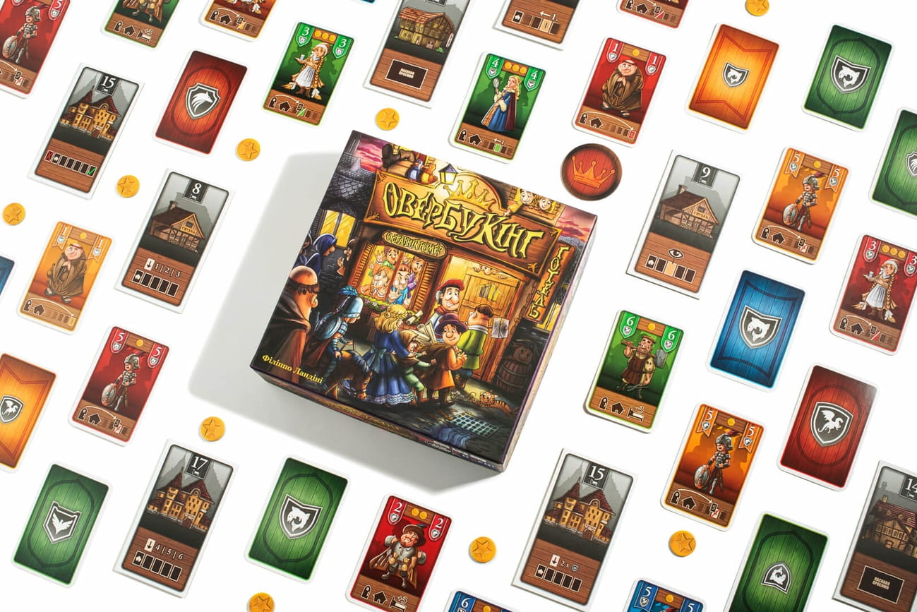 Настольная игра Овербукінг от SOVABOOKS для детей, изображена коробка с игровыми компонентами и ярким дизайном